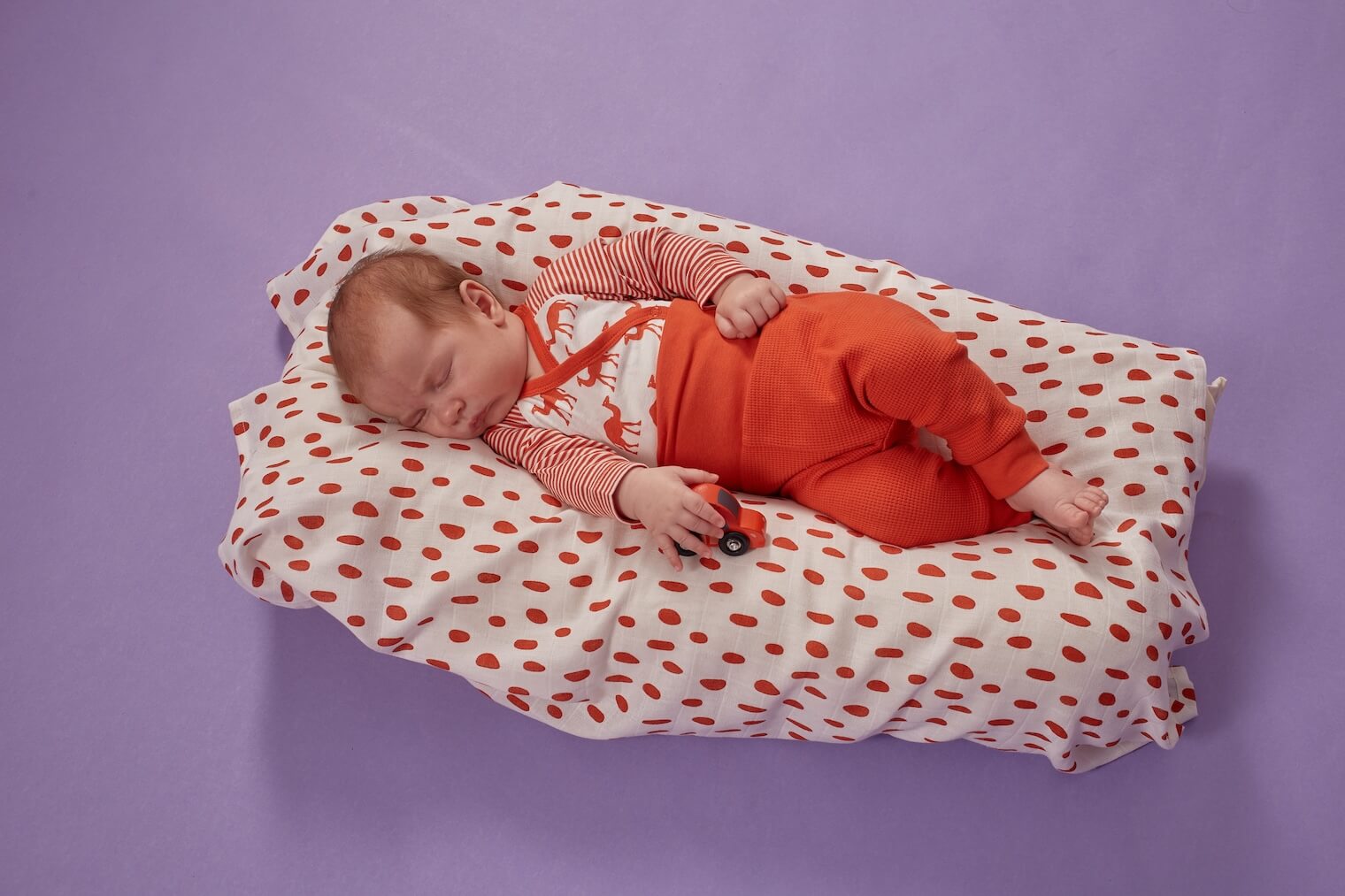 Baby mit Spielzeugauto liegt auf weichem Bett und schl&auml;ft