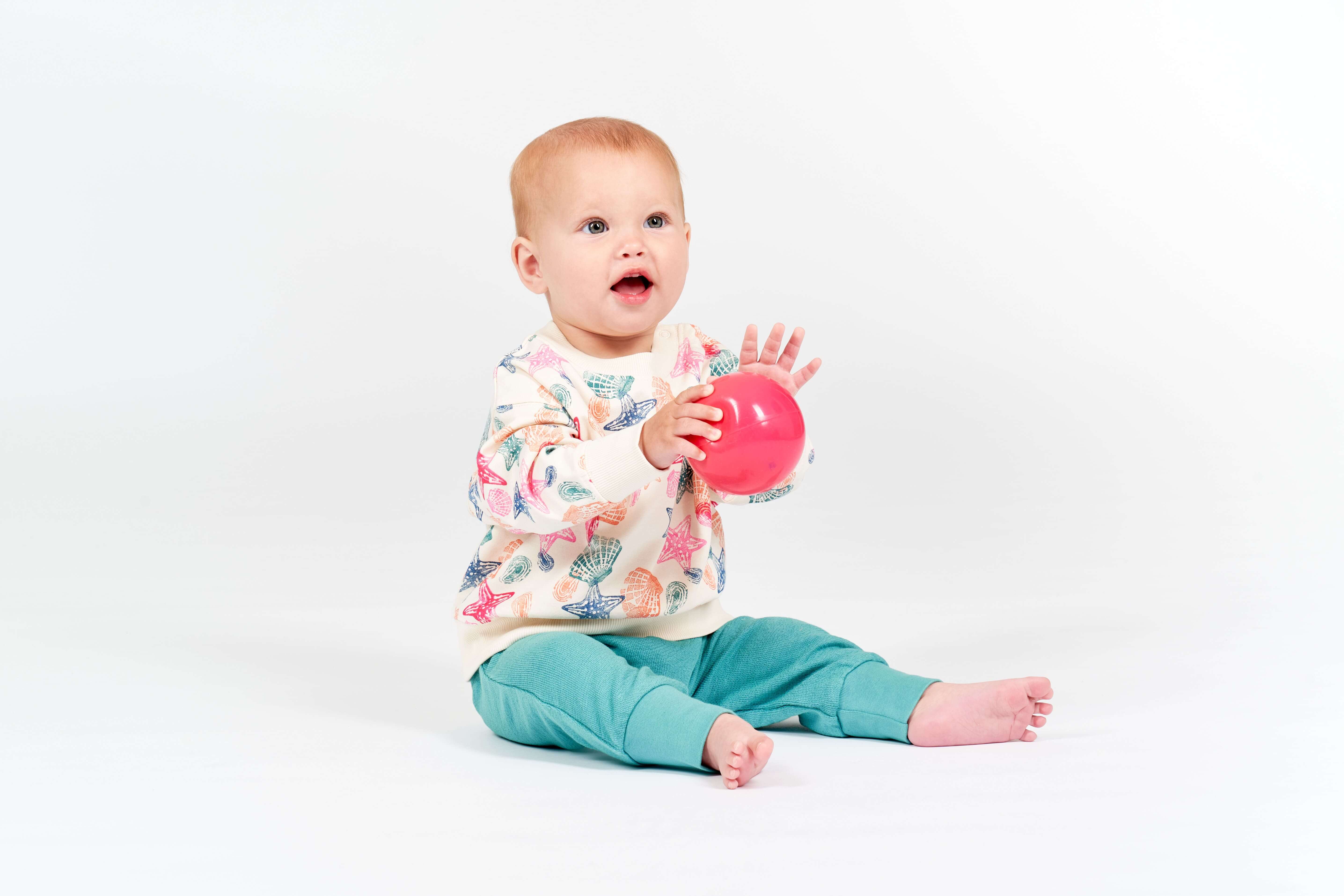 Baby mit coolem Outfit h&auml;lt Ball in der Hand